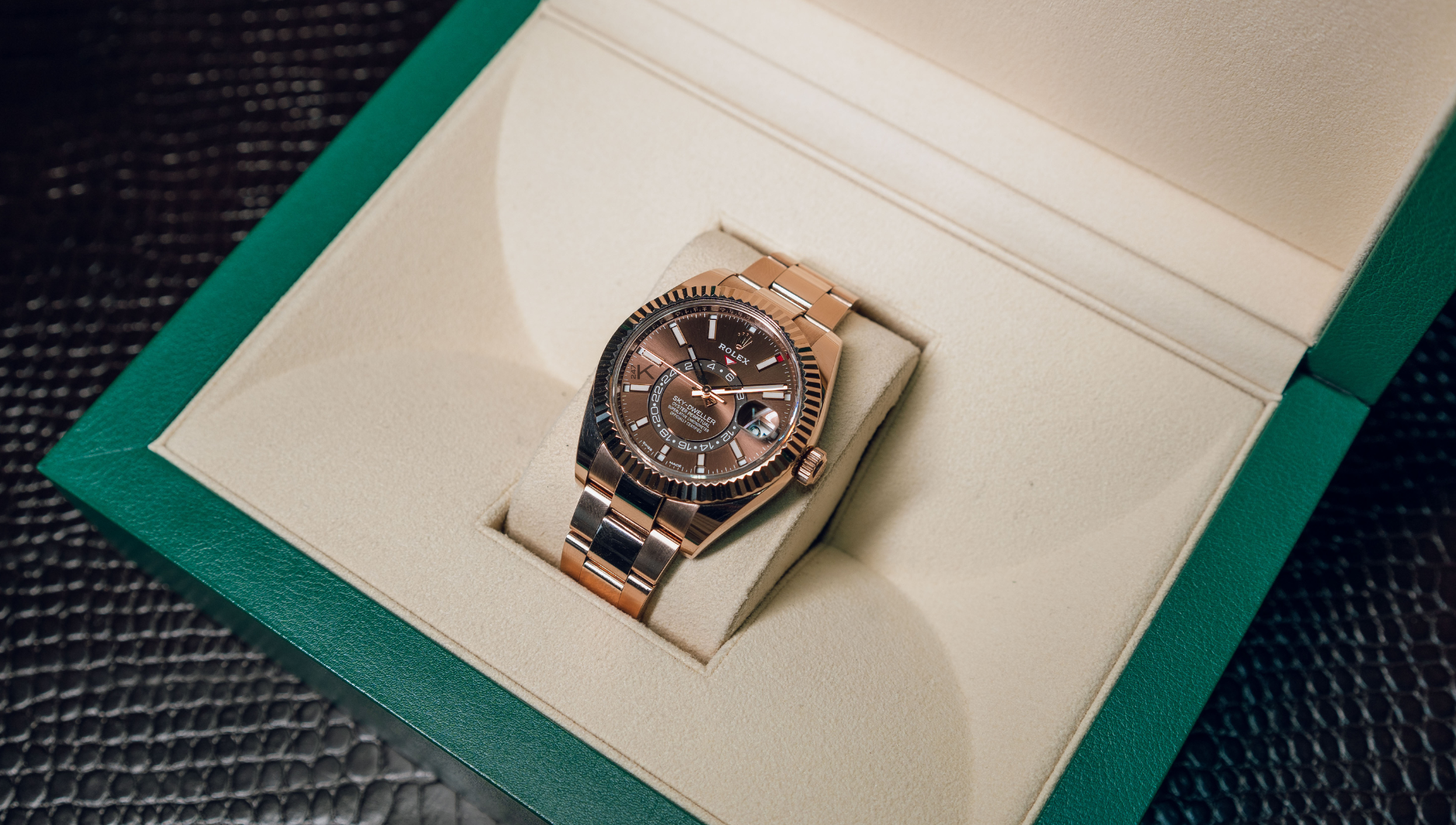 Luxury watch with a gold and black design inside an open green and beige box, resting on a textured leather surface, exuding elegance and sophistication.