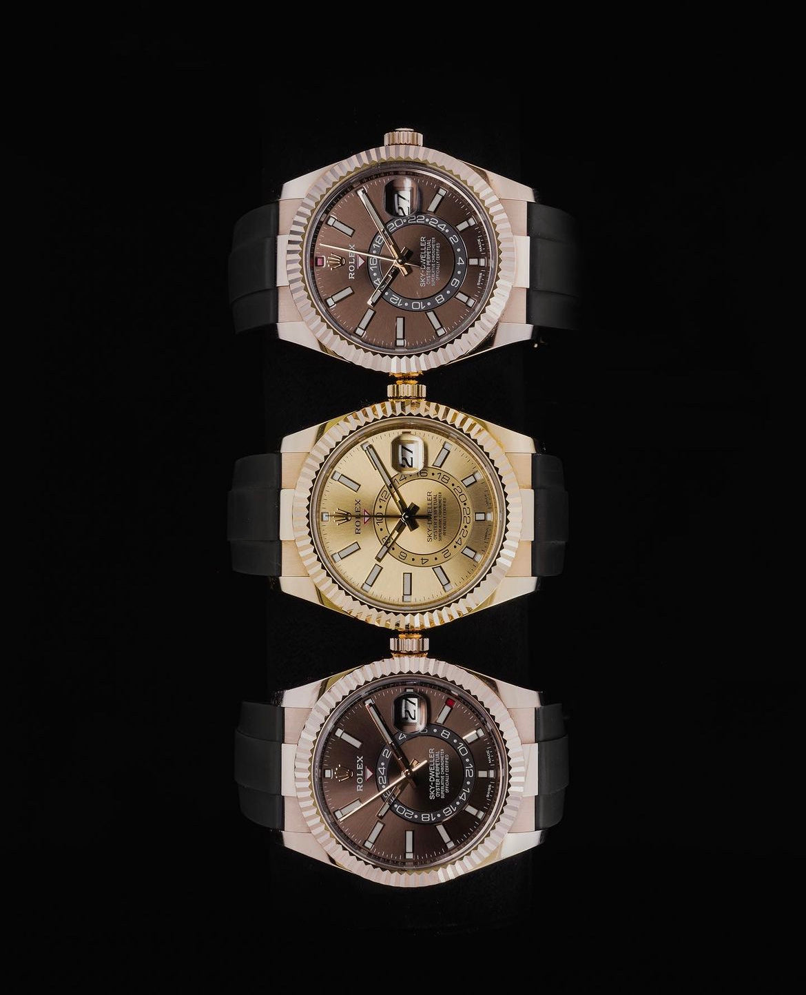 Three luxury watches with metallic bezels and dark dials are aligned vertically against a black background. Each watch features a sleek, modern design.
