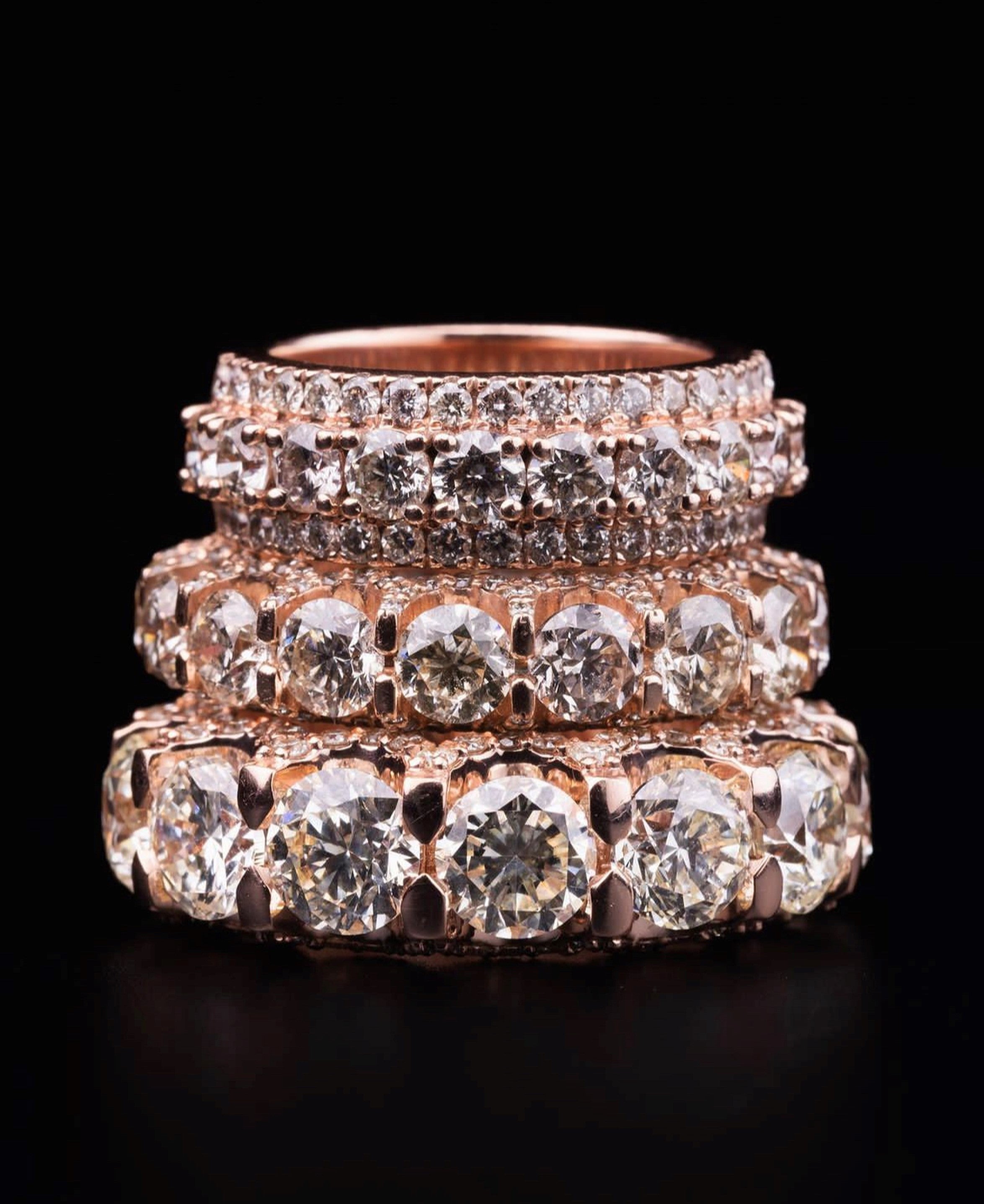 Three rose gold rings stacked, each encrusted with sparkling diamonds, displayed against a black background, conveying elegance and luxury.